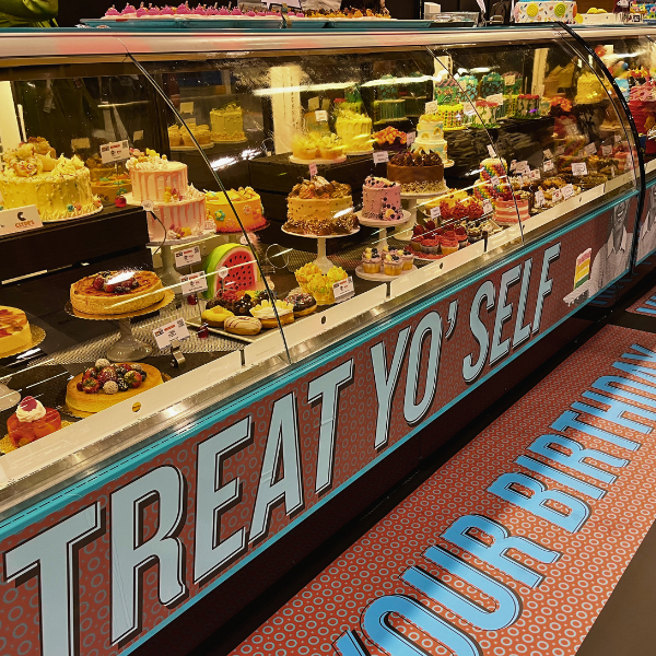 A large refrigerated display case filled with various pastries and desserts. The display case has a custom sign and matching floor decal.